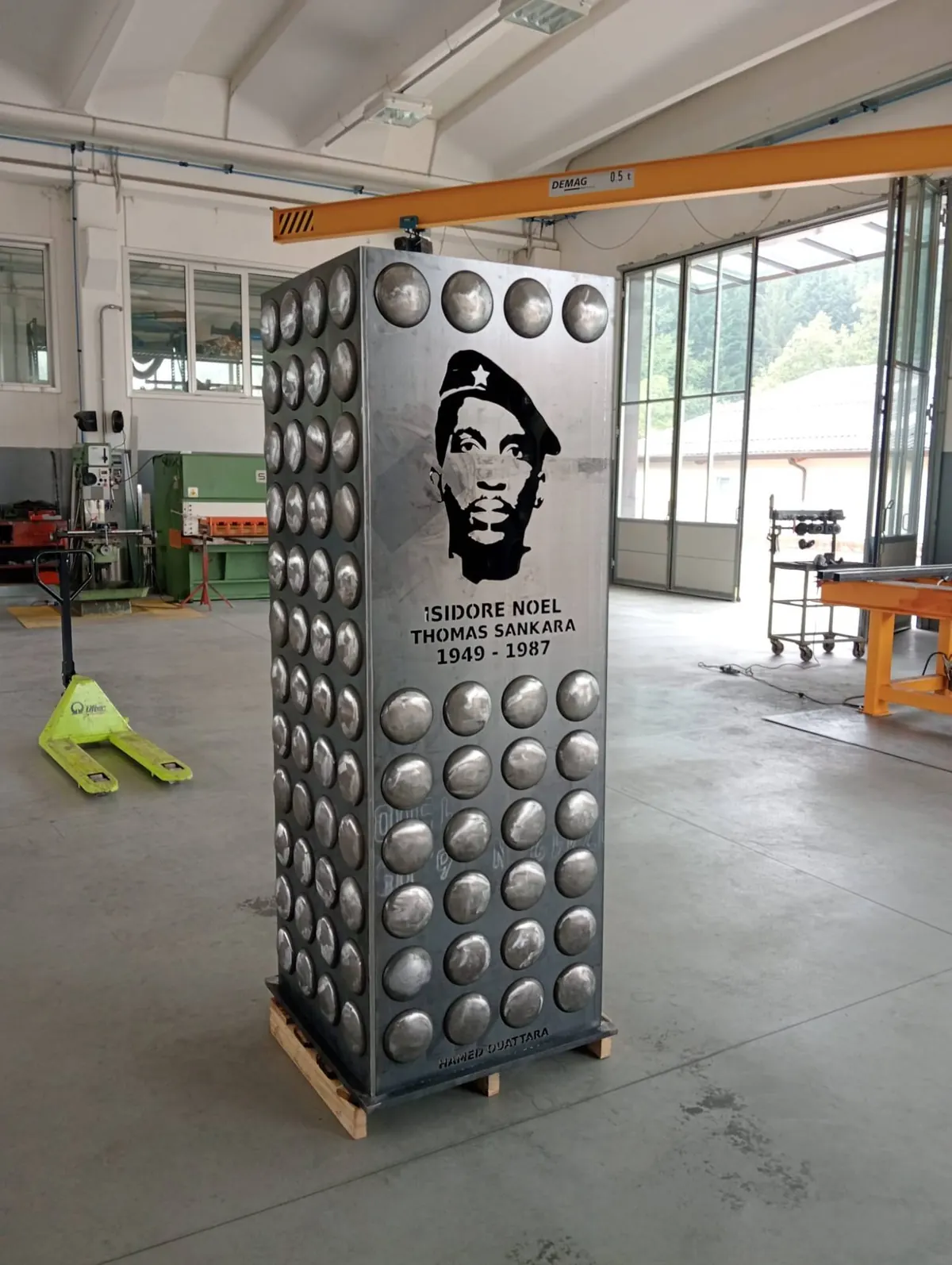 Le prisme de SANKARA, L'ÉTERNEL VEILLEUR de Hamed Ouattara en acier brut, avant oxydation, dans l'atelier de Bologne : les bossages hémisphériques accrochent la lumière et le visage découpé se détache en noir.