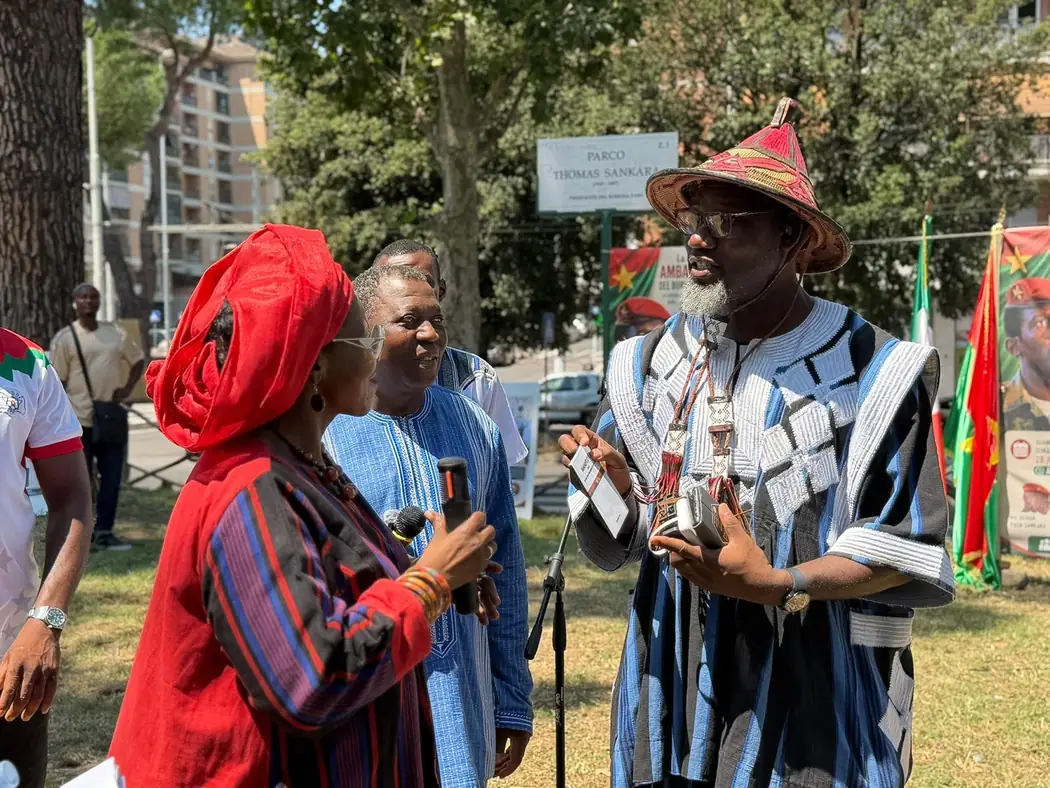 Rencontre préparatoire au Parco Thomas Sankara de Rome : des représentants de la communauté burkinabè s'adressent à la presse devant la plaque du parc et les drapeaux du Burkina Faso.